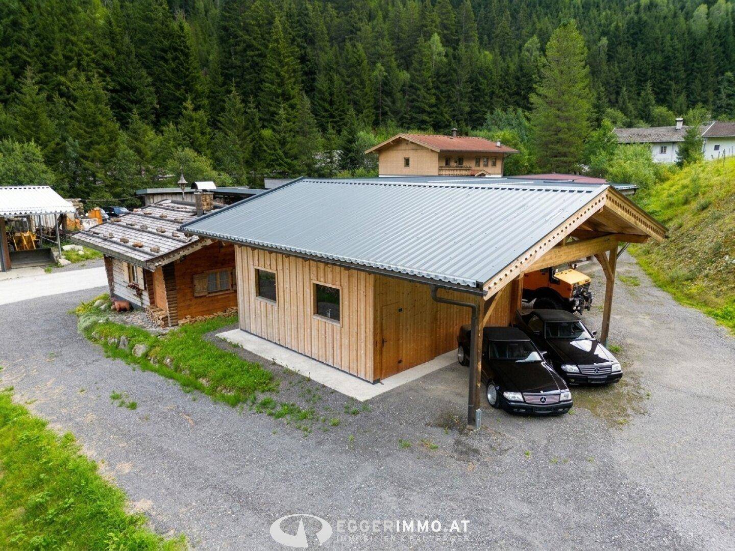 Neues Holzgebäude mit integriertem Carport und einer charmanten traditionellen Holzhütte daneben.