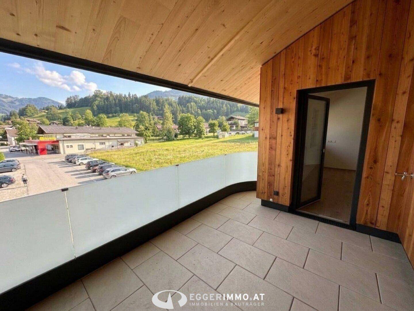 Sonniger Balkon mit Fliesenboden, Glasbrüstung und Panoramablick auf die Berge.