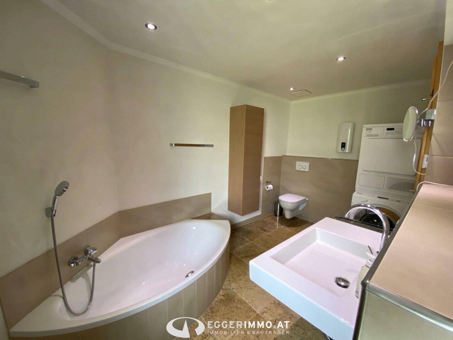 Geräumiges Badezimmer mit Badewanne, Waschbecken und integrierter Waschmaschine.