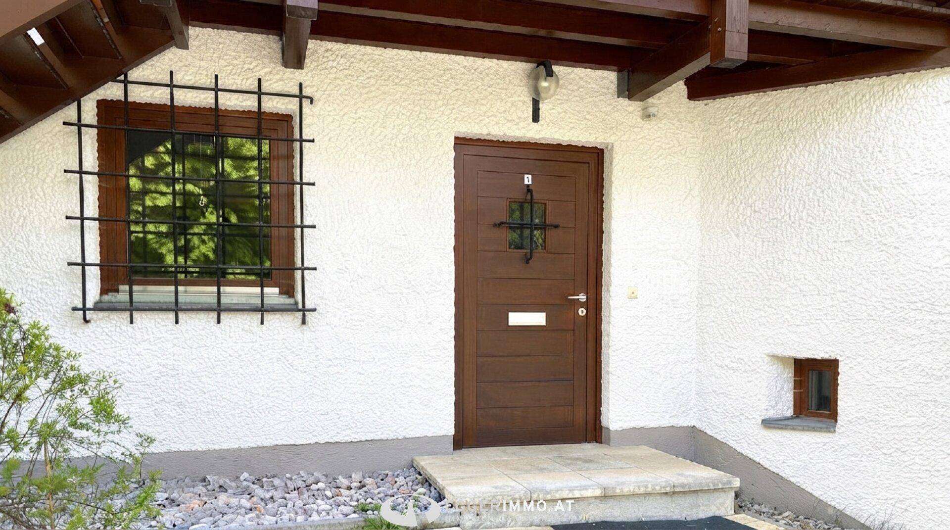 Eingangsbereich des Hauses mit Holztür, Fenster und dekorativem Gitter.