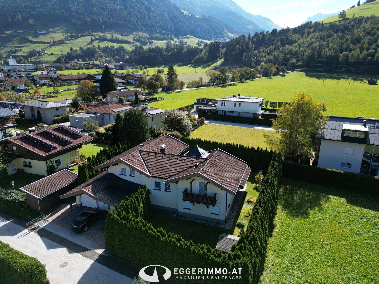 Luftaufnahme eines Hauses mit Garten und Carport in einer grünen Berglandschaft.