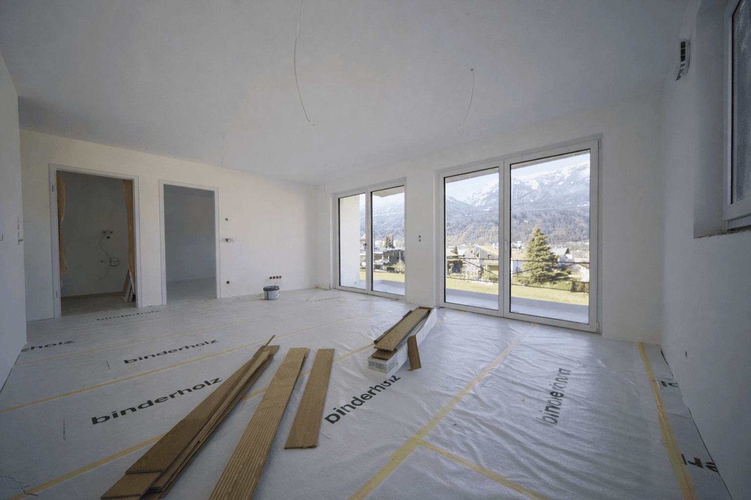 Geräumiger Wohnraum im Neubau mit vorbereitetem Boden für Holzdielen und Bergblick.
