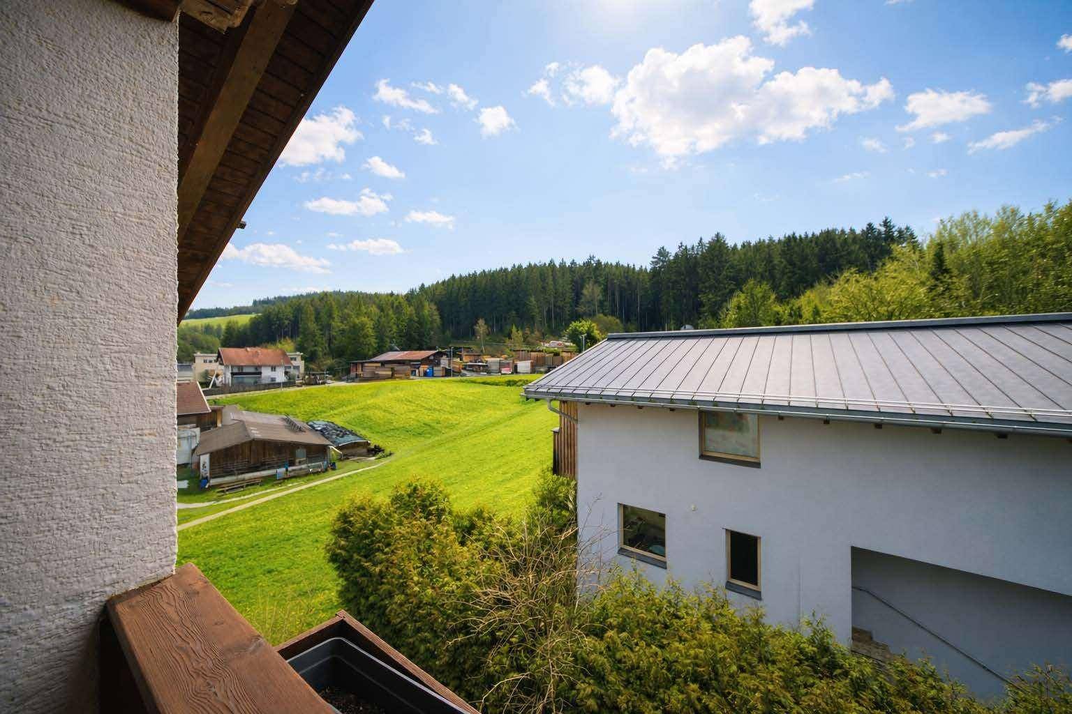 Malerischer Ausblick vom Balkon auf grüne Hügel und bewaldete Landschaft unter blauem Himmel.