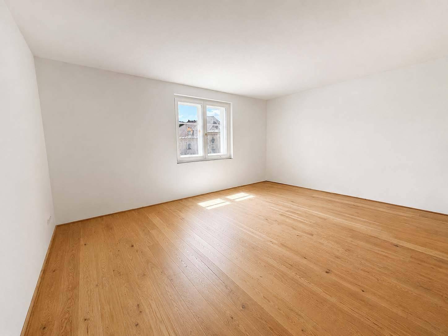 Großes Schlafzimmer mit Parkettboden und viel Tageslicht durch das Fenster.