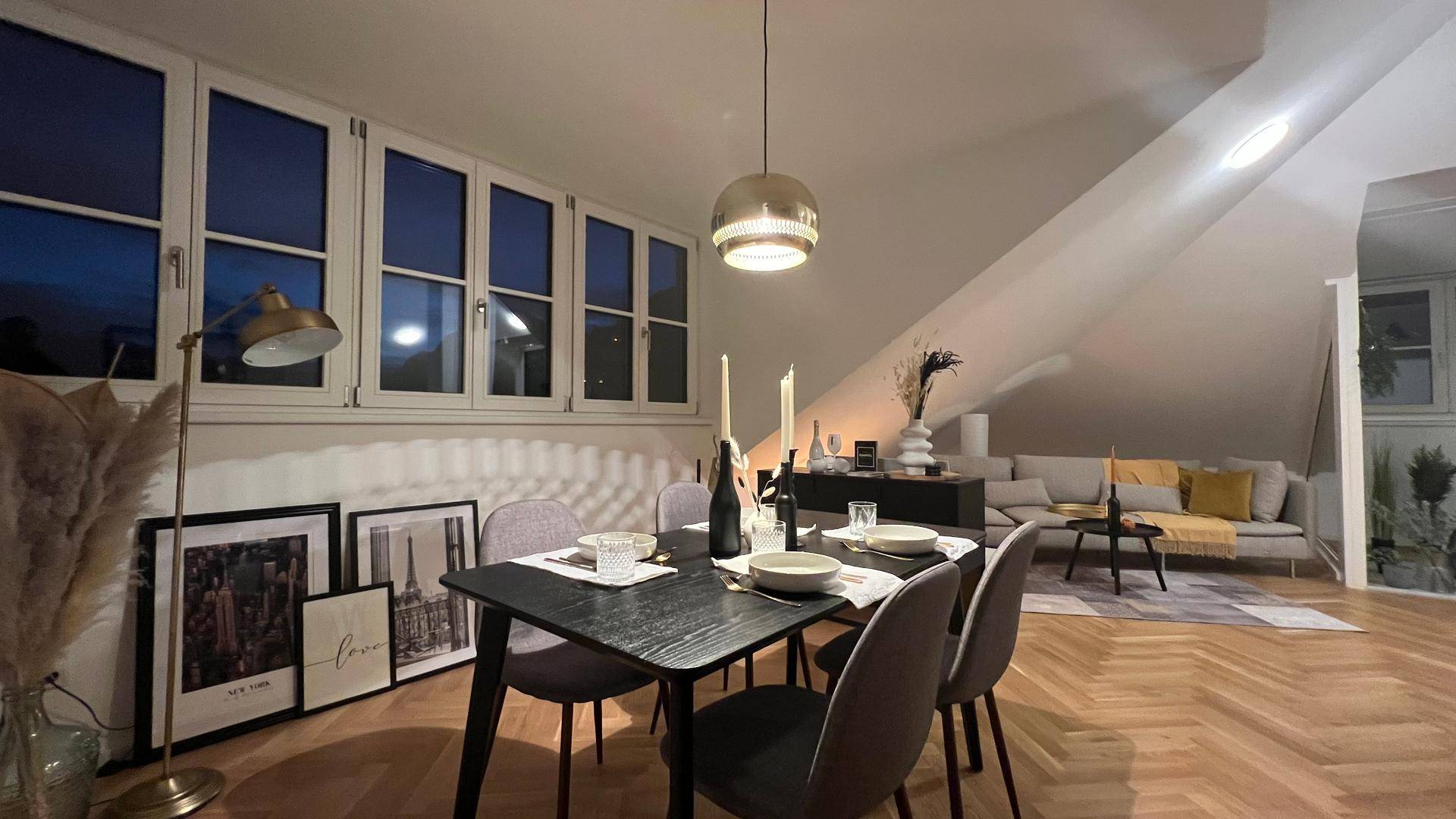 Gemütlicher Wohn-Essbereich am Abend mit Esstisch, Sofa und schrägen Dachfenstern.