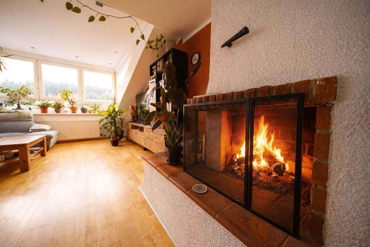 Gemütlicher Wohnbereich mit Kamin, Holzboden und Blick auf die grüne Umgebung durch große Fenster.