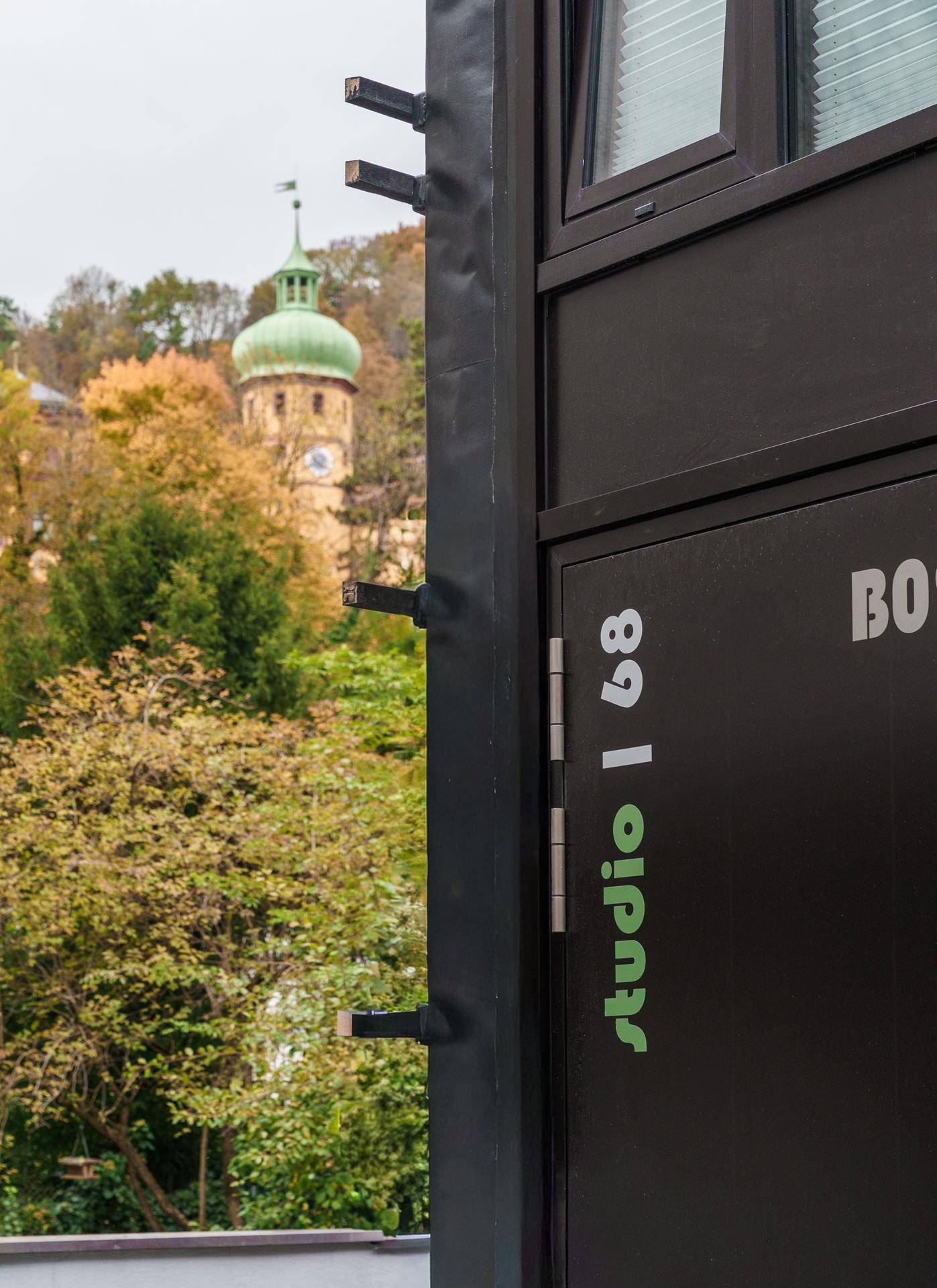 Detailansicht der modernen Fassade mit Blick auf einen historischen Kirchturm und herbstliche Bäume.