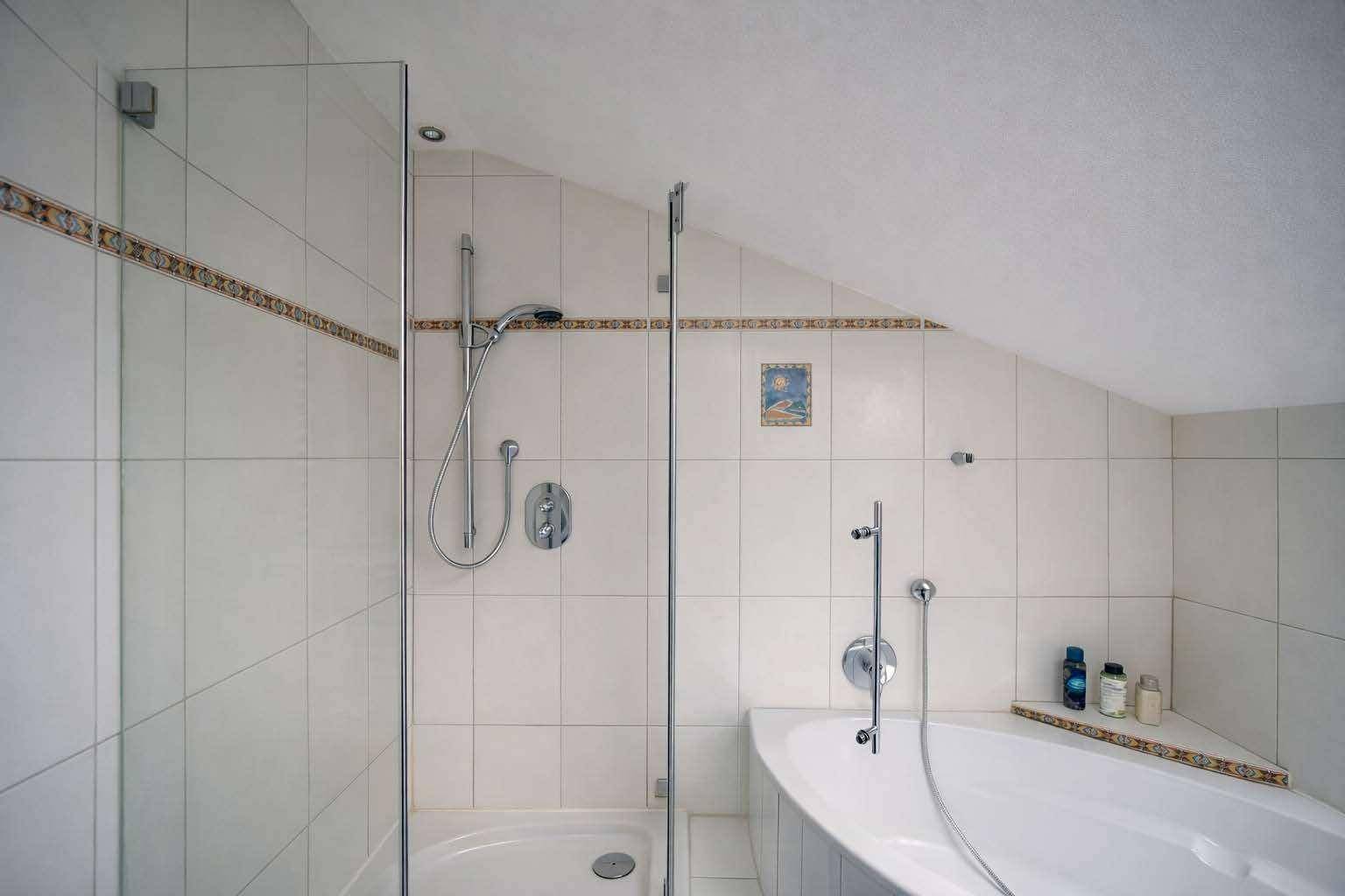 Duschbereich im Badezimmer mit Glasabtrennung und Badewanne unter der Dachschräge.
