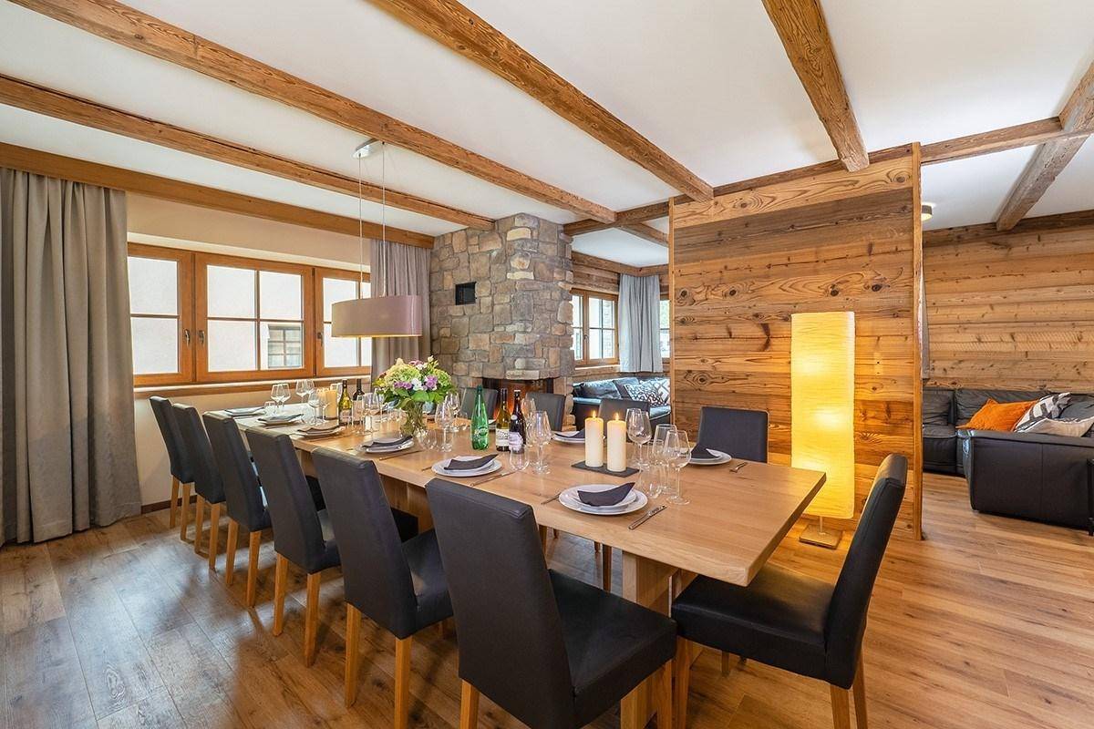 Festlich gedeckter Essbereich mit großem Holztisch, Steinwandkamin und Holzbalkendecke.