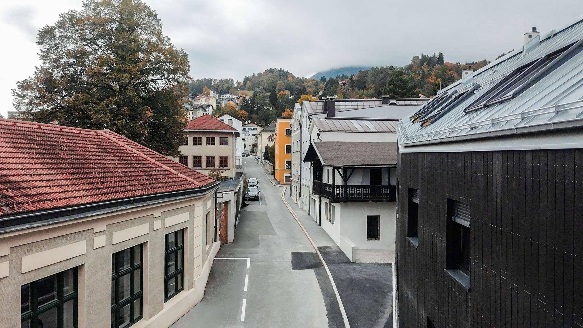 Blick von oben auf eine Wohnstraße mit verschiedenen Gebäuden und herbstlicher Landschaft.