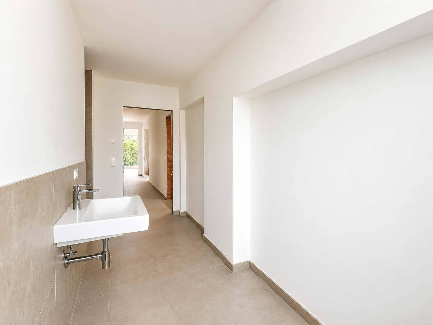 Modernes Gäste-WC mit Wandwaschbecken und hellen Fliesen an den Wänden.