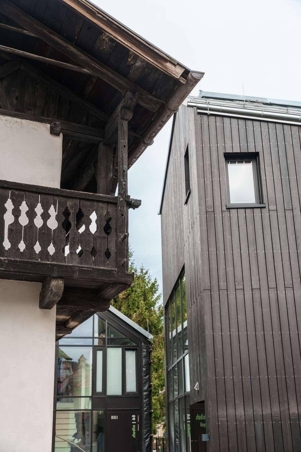 Kontrast zwischen traditionellem Holzhaus mit Balkon und moderner Holzfassade.