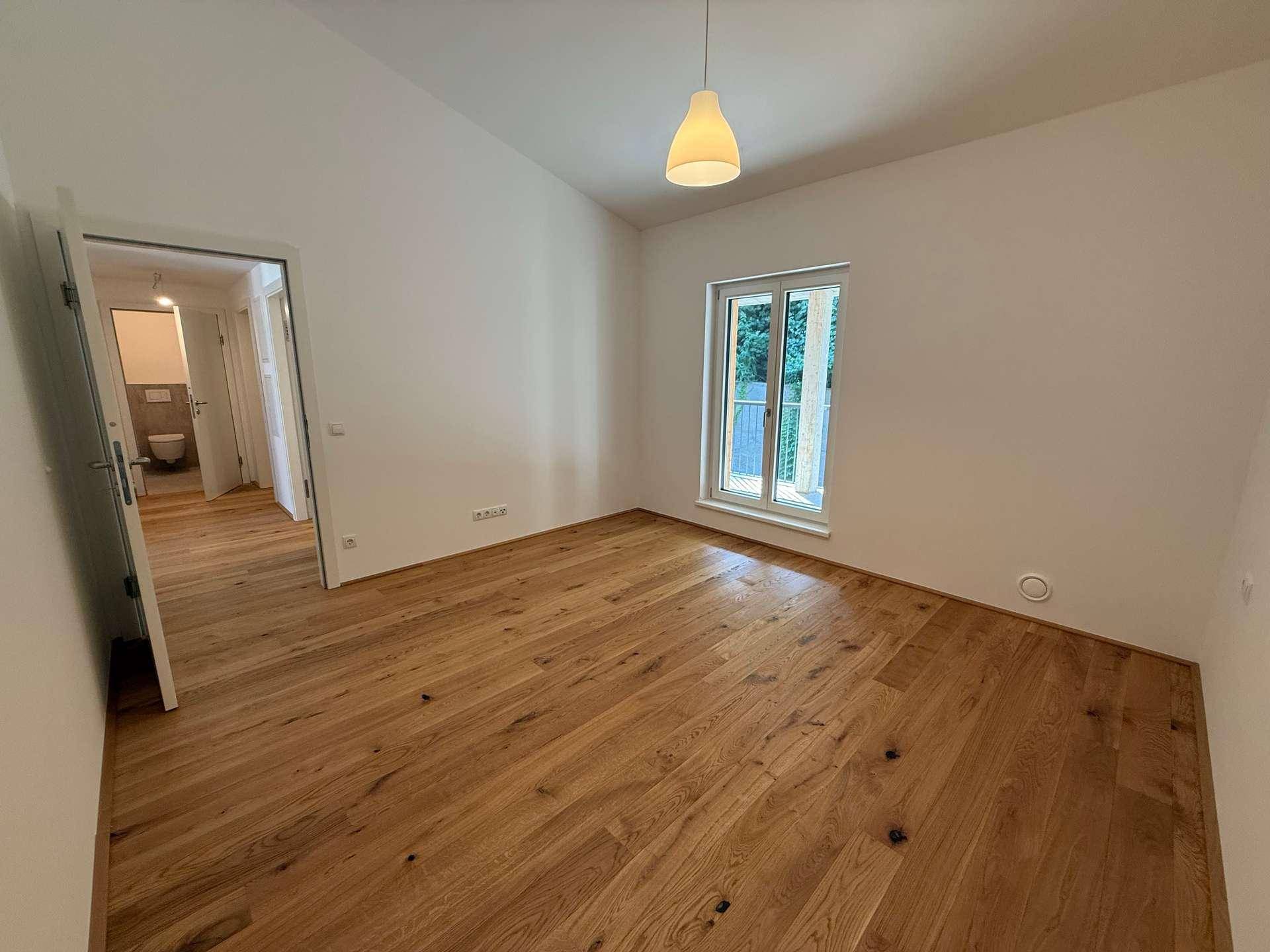 Schlafzimmer mit Holzboden, Fenster und Blick auf ein angrenzendes Badezimmer.
