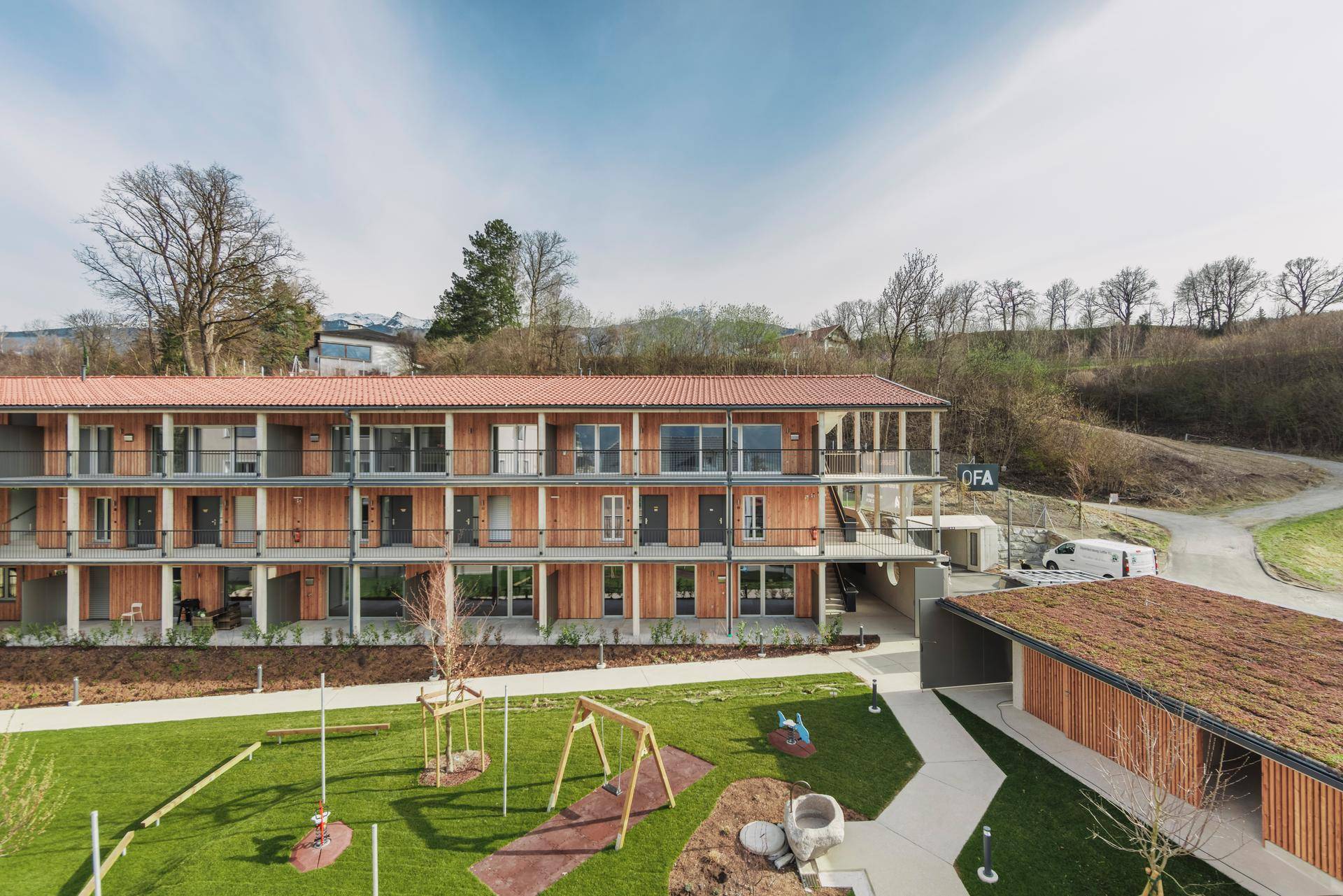 Modernes Mehrfamilienhaus mit Holzfassade, Balkonen und einem Spielplatz im Vordergrund.