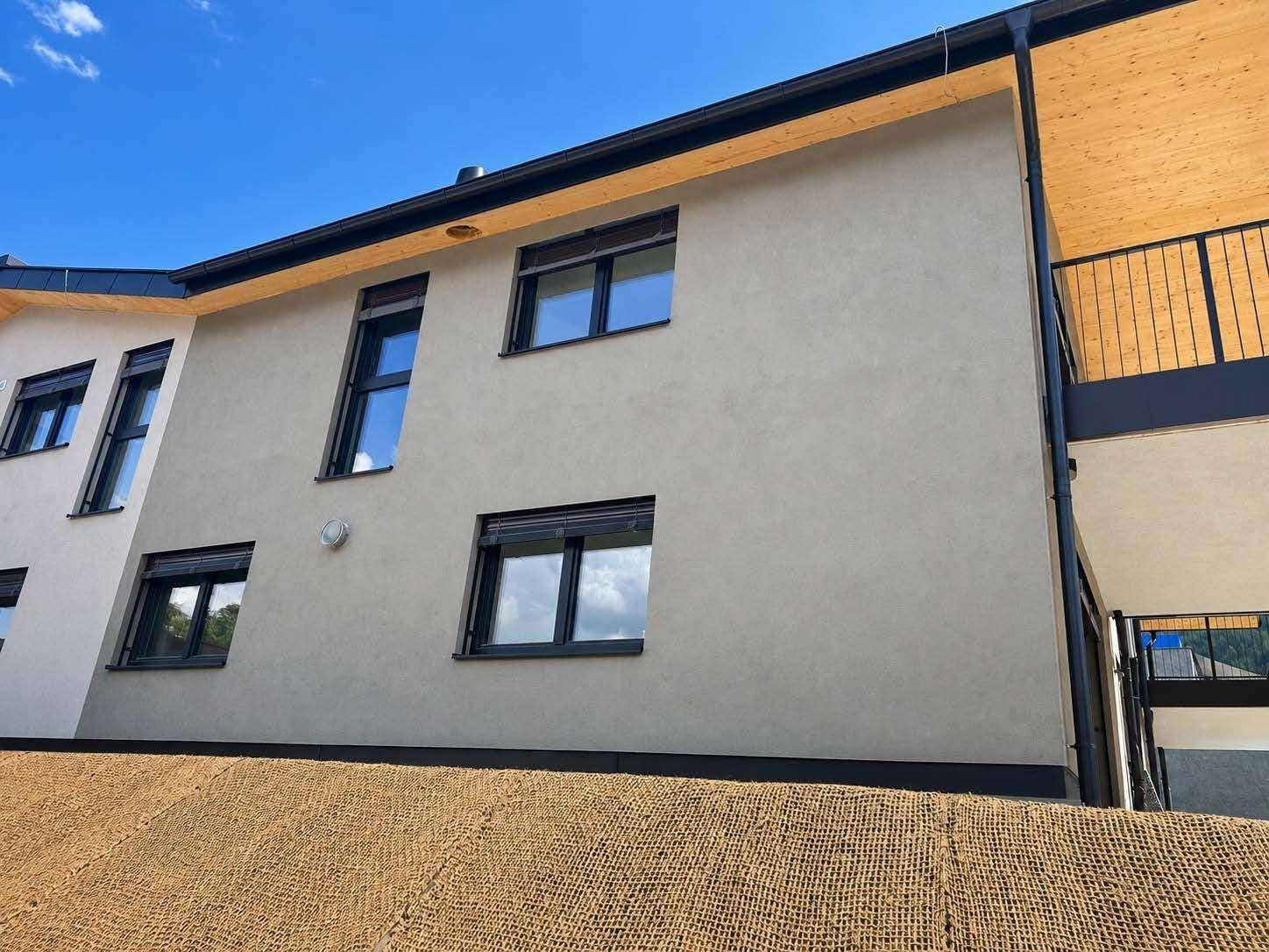 Detailansicht der modernen Fassade mit Fenstern, Rollläden und Holzverkleidung.