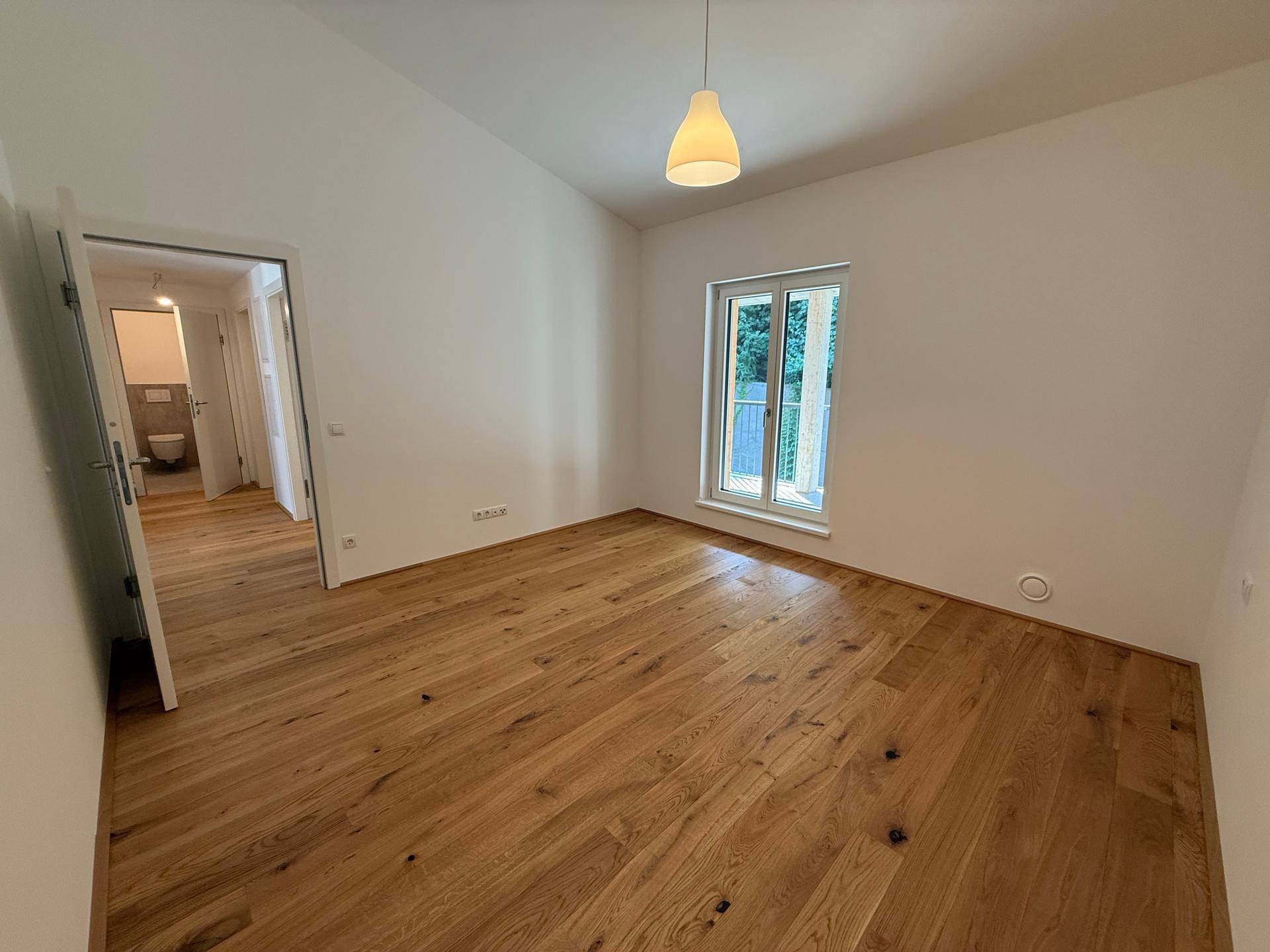 Schlafzimmer mit Holzboden und Zugang zu einem angrenzenden Badezimmer, hell und modern.