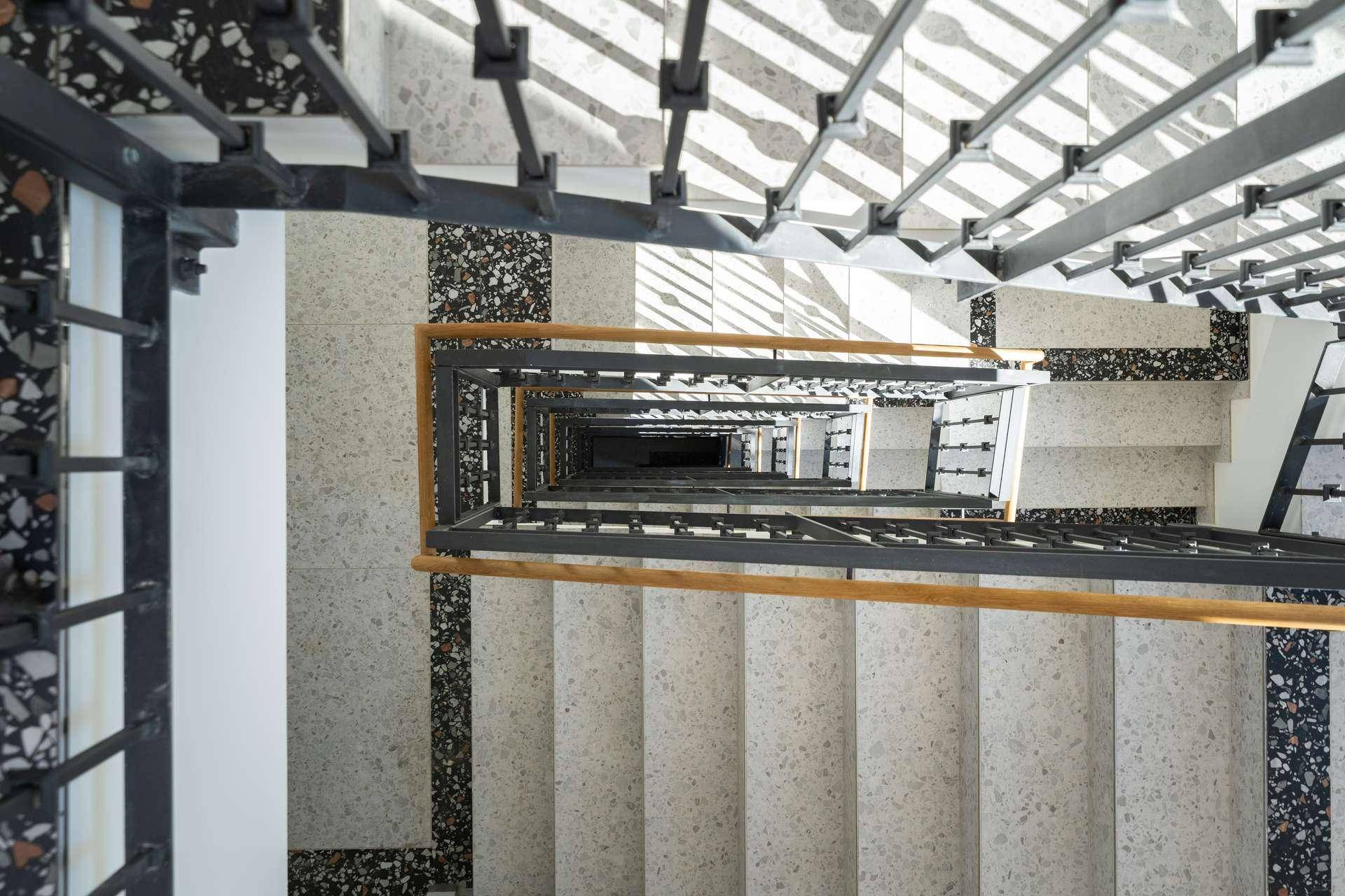 Modernes Treppenhaus mit Terrazzoboden und Metallgeländer in einem Mehrfamilienhaus.