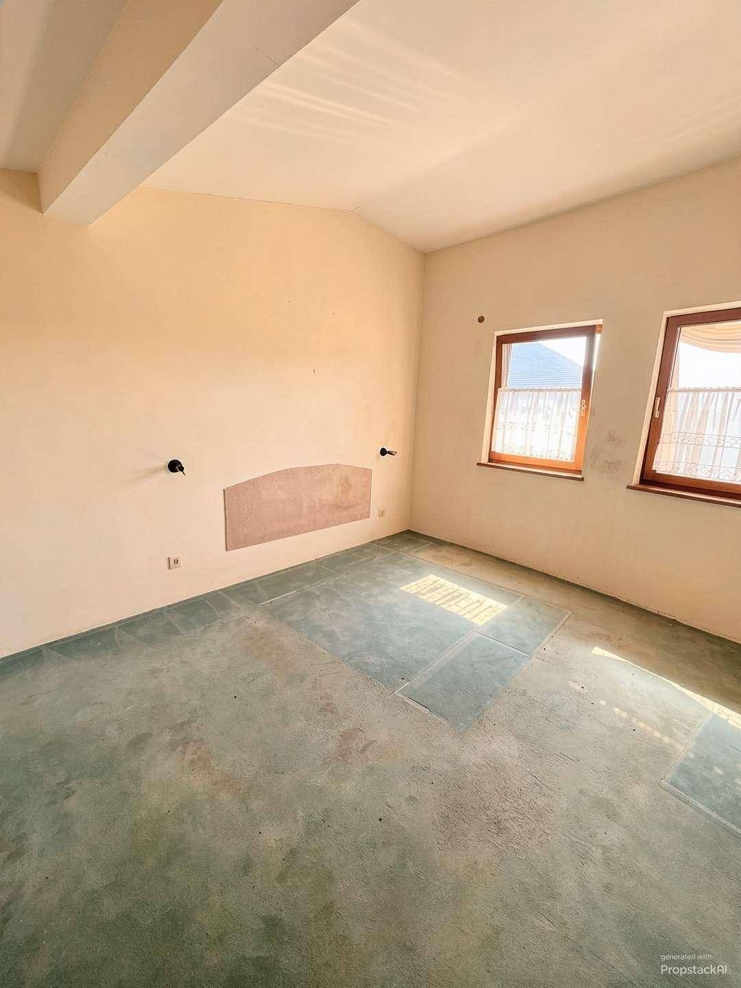 Unmöbliertes Schlafzimmer mit Teppichboden, zwei Fenstern und einer Dachschräge, die Gemütlichkeit schafft.
