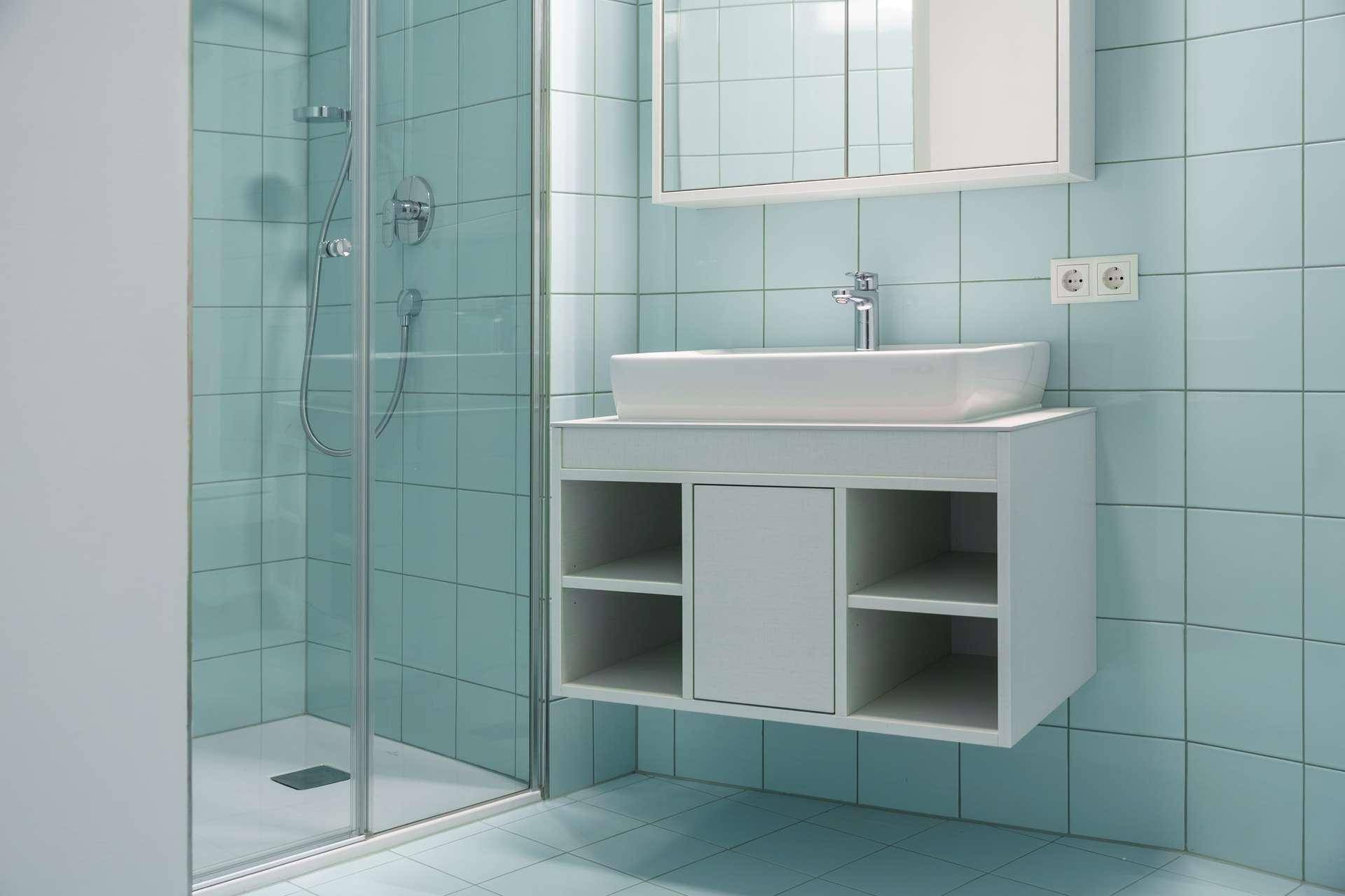 Modernes Badezimmer mit hellblauen Fliesen, Duschkabine und schwebendem Waschtisch.