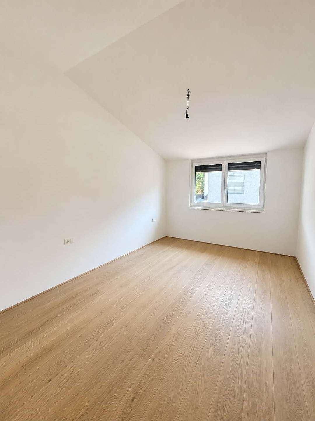 Geräumiges Schlafzimmer mit Holzboden und Fenster, bietet viel natürliches Licht.