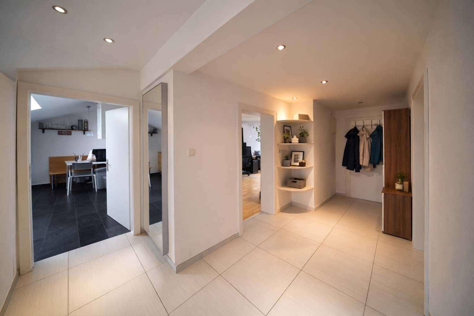 Heller Flur mit Fliesenboden, Einbauregal und Garderobe, der zu weiteren Räumen führt.