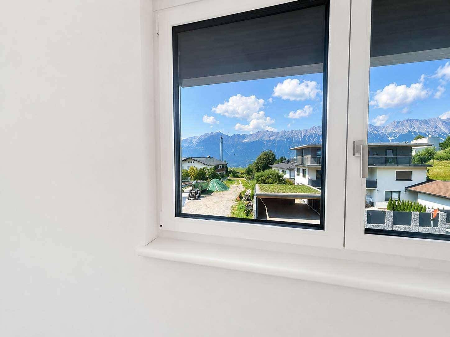 Fensterblick auf die umliegende Berglandschaft und benachbarte Häuser.