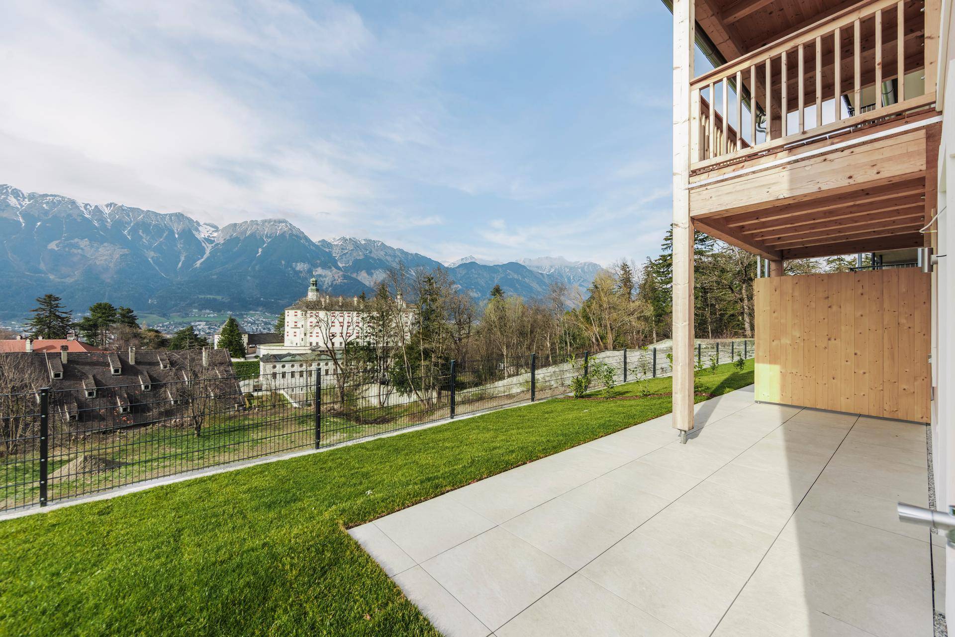 Sonniger Terrassenbereich mit Rasenfläche und weitem Blick auf die Berge und ein historisches Gebäude.
