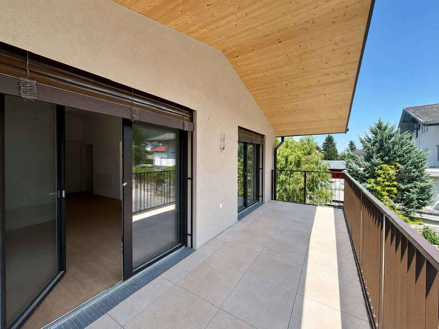 Geräumiger Balkon mit Fliesenboden, Holzdecke und Blick ins Grüne.