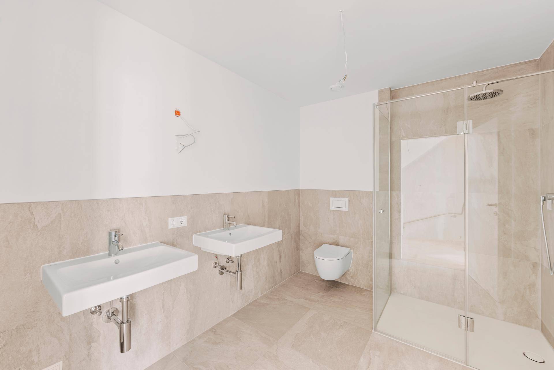 Geräumiges Badezimmer mit zwei Waschbecken, Duschkabine und wandhängendem WC.