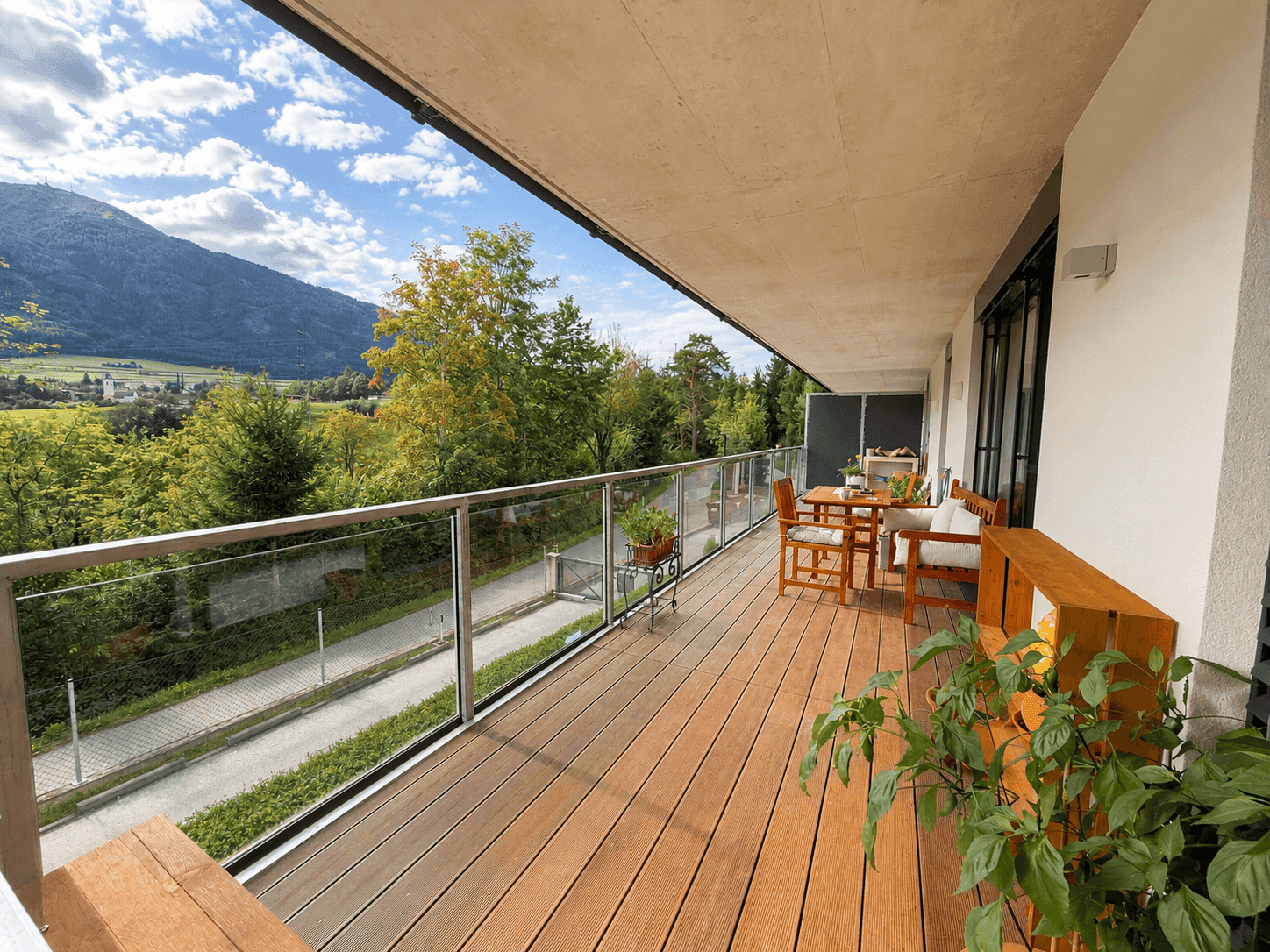 Großer Balkon mit Holzboden, Glasgeländer und weitem Blick auf die Berge und Landschaft.