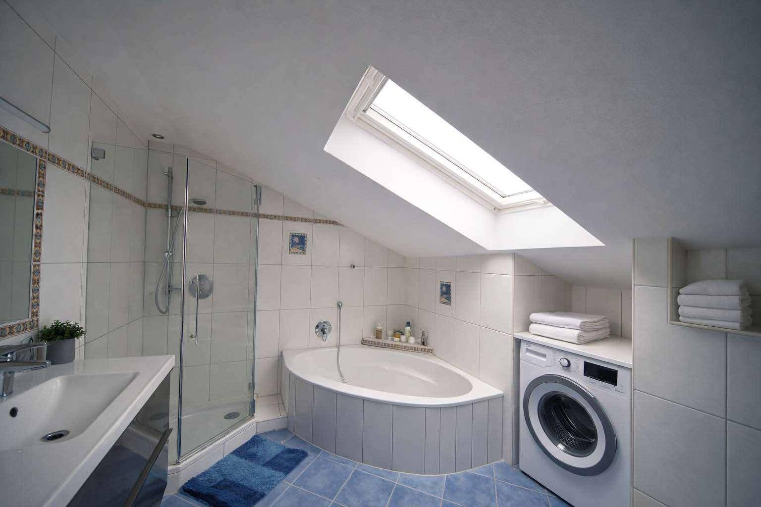 Modernes Badezimmer mit Badewanne, Dusche, Waschmaschine und Dachfenster für viel Licht.