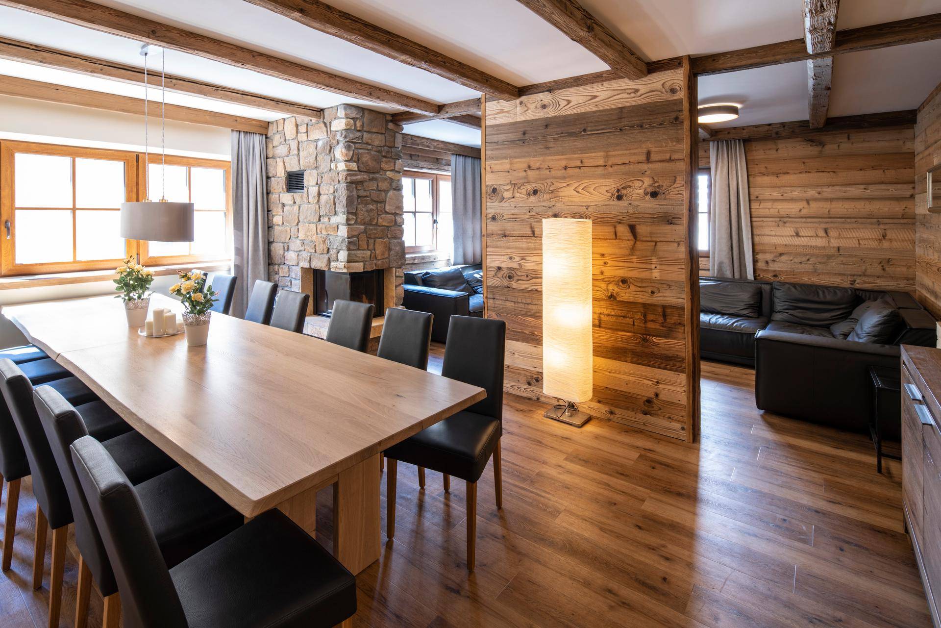 Heller Essbereich mit großem Holztisch, Steinwand und rustikalen Holzbalken an der Decke.