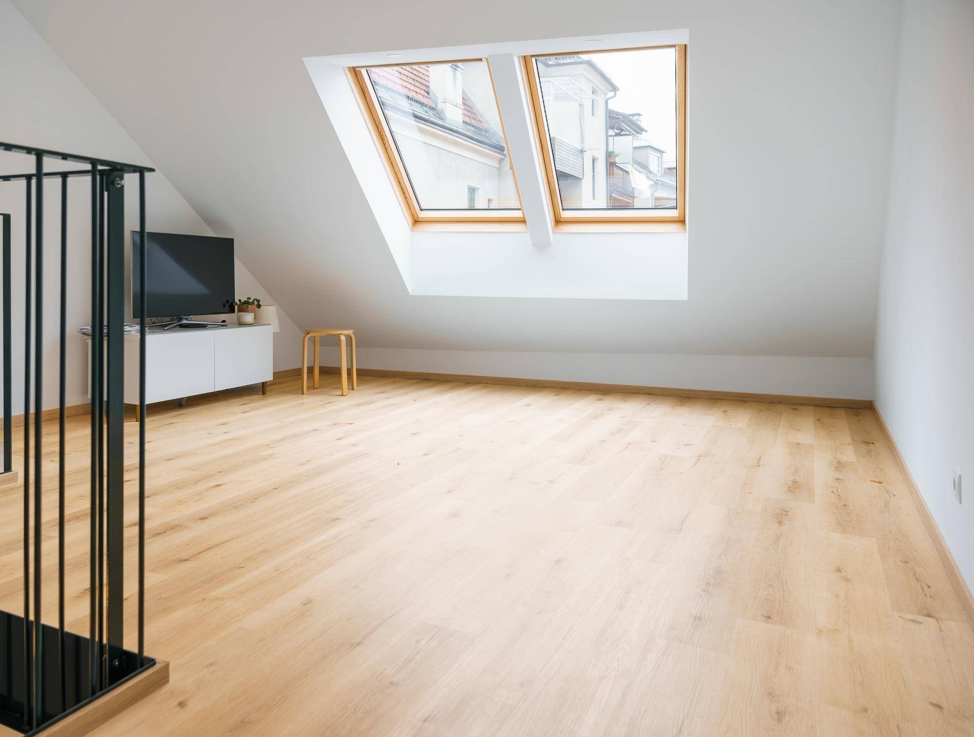 Wohnraum mit Dachschrägen, Holzfußboden, zwei Dachfenstern und einem TV-Möbel.