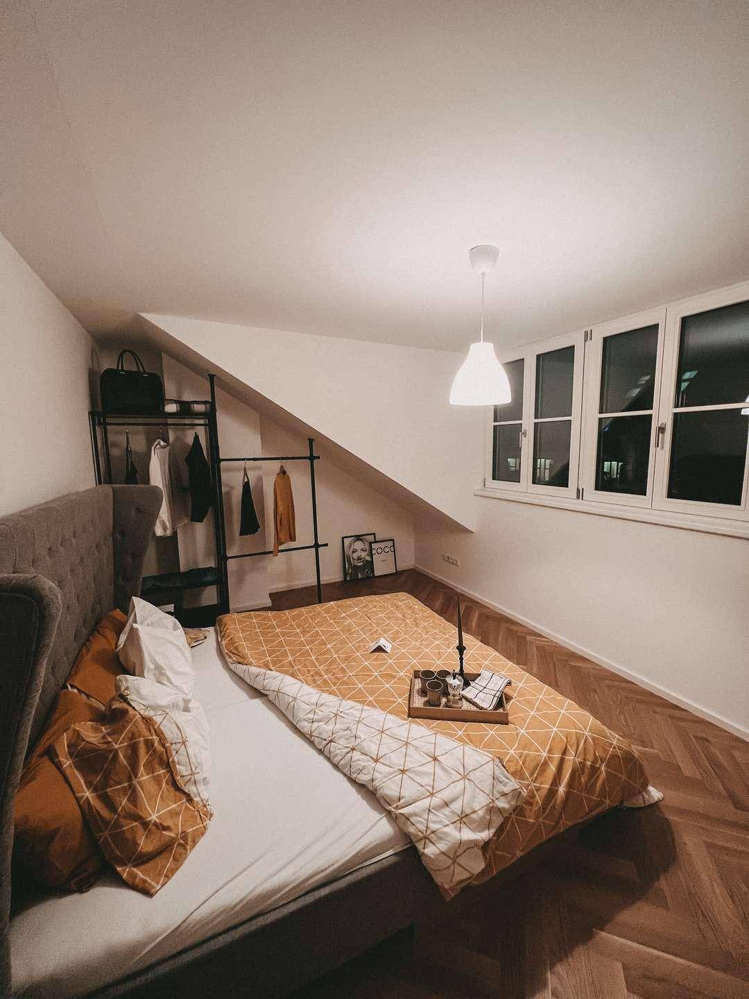 Gemütliches Schlafzimmer mit Bett, offenem Kleiderschrank und Fenstern unter der Dachschräge.
