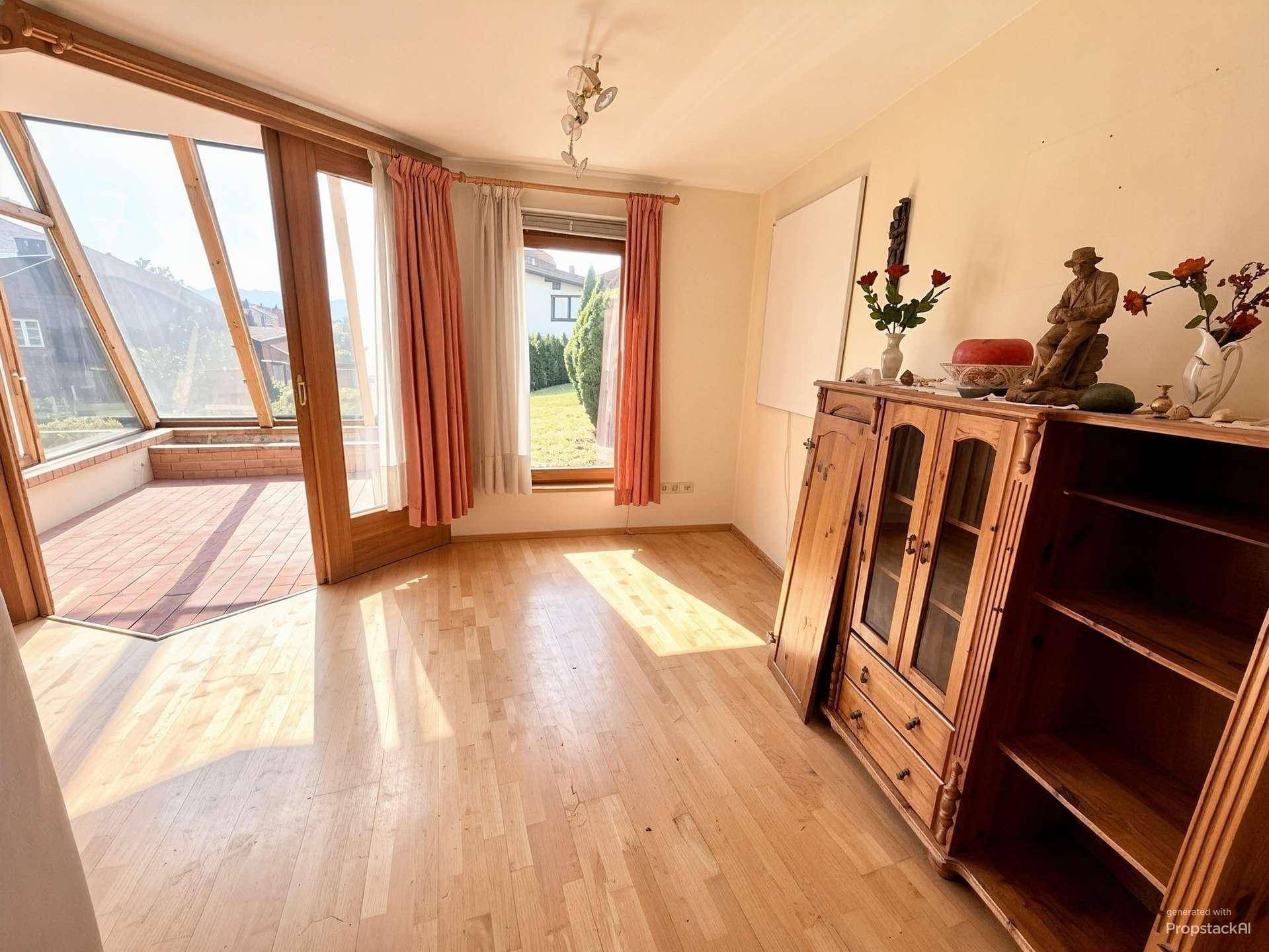 Unmöblierter Raum mit Holzboden und großen Glastüren, die zu einem sonnigen Wintergarten führen.