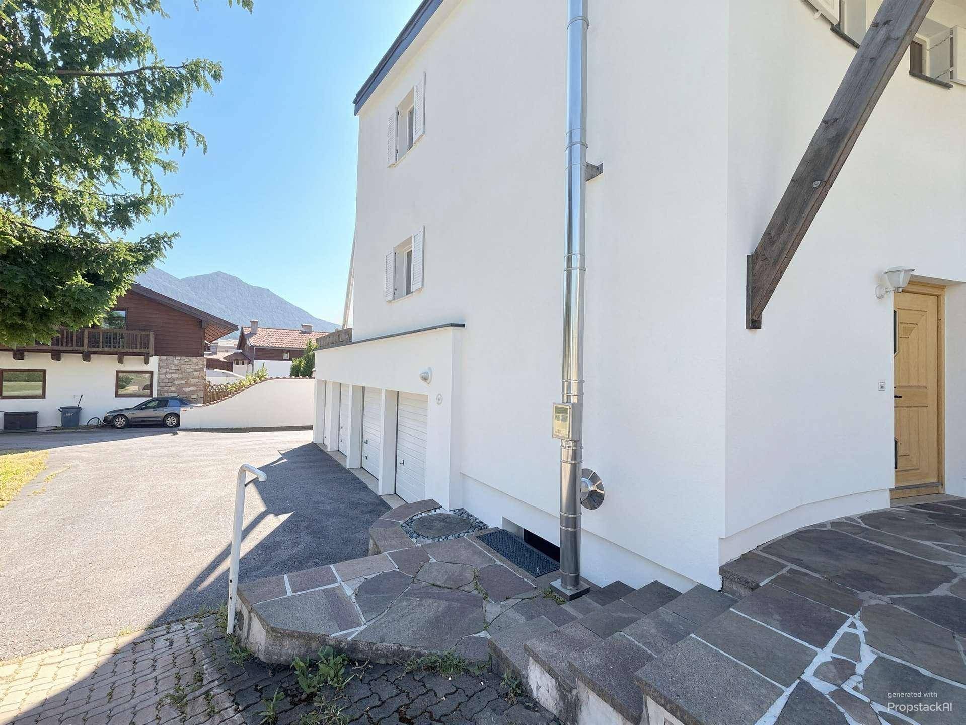 Seitenansicht des Hauses mit Garagenzugang und einem Edelstahlkamin, umgeben von Natur.