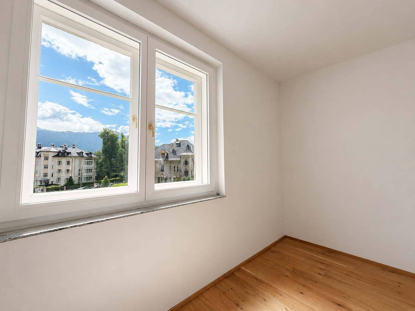 Helles Schlafzimmer mit Parkettboden und weitem Blick auf die Stadt und Berge.