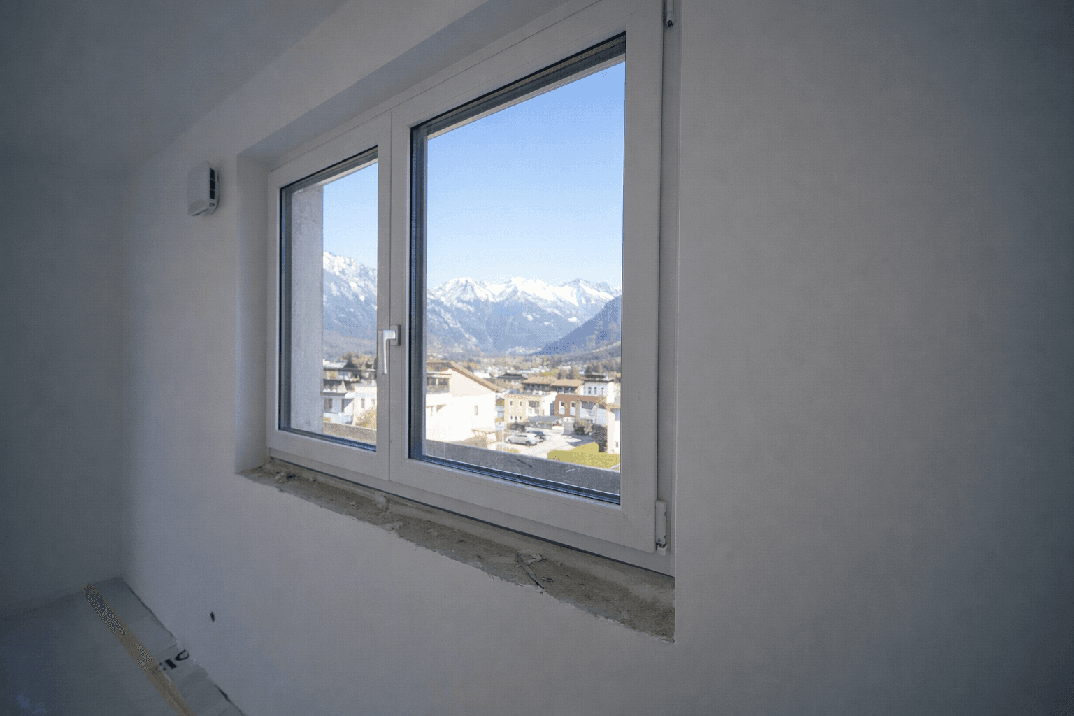 Fenster in einem unfertigen Raum mit klarem Blick auf die schneebedeckten Berge und die Stadt.