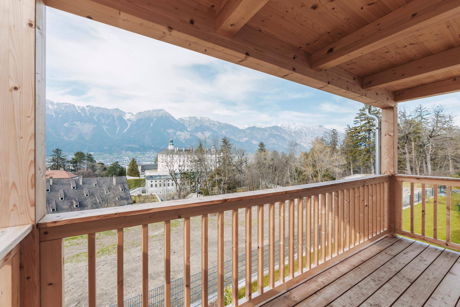 Geräumiger Holzbalkon mit Geländer und weitem Blick auf die Berglandschaft und das Tal.