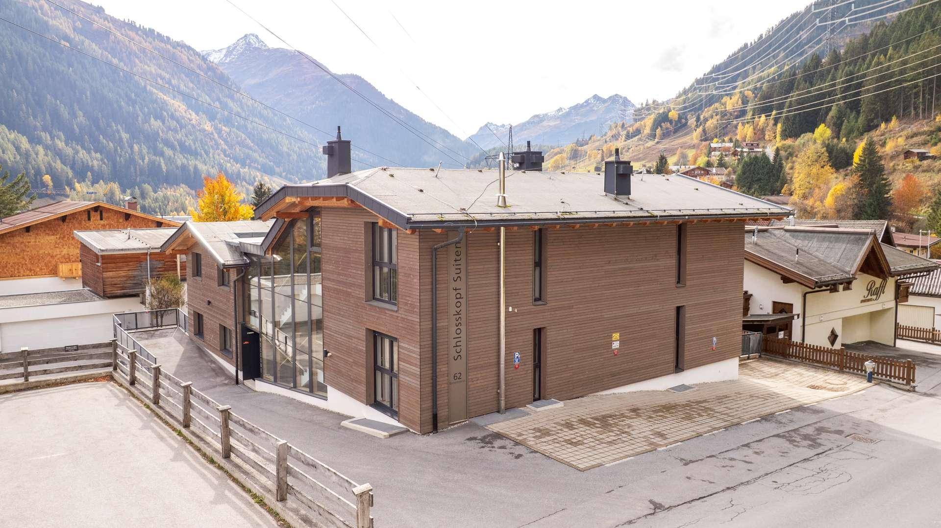 Vorderansicht des modernen Gebäudes mit Holzfassade, Glasfront und Bergblick.