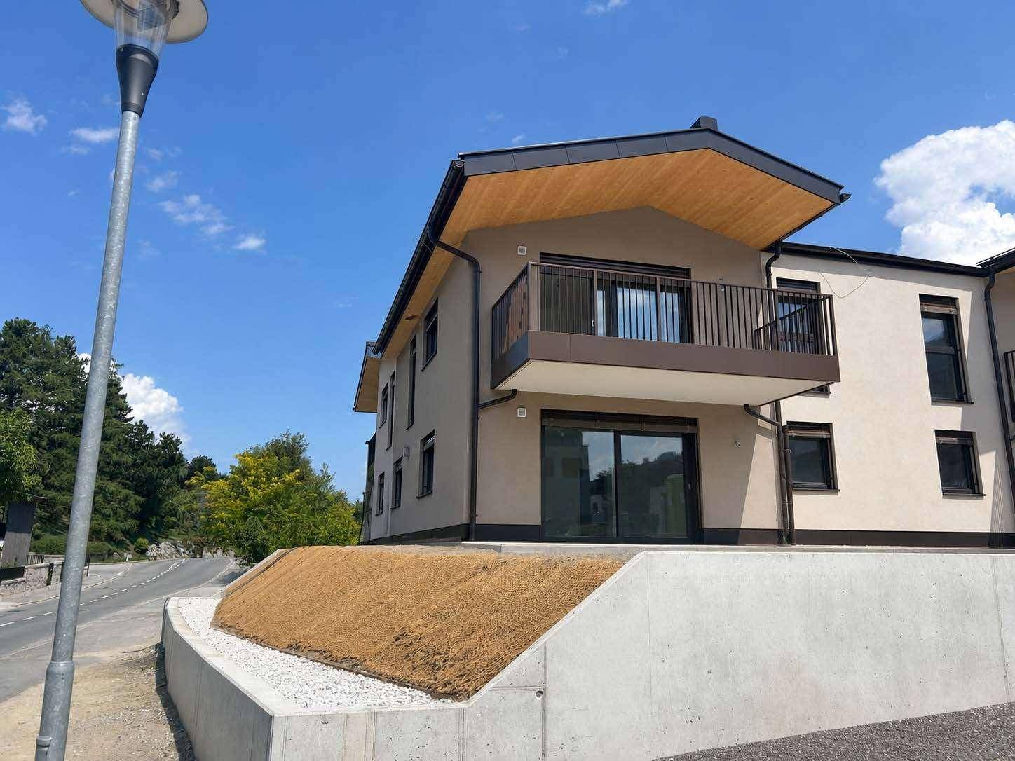 Moderne Gebäudefassade mit Balkon und schräger Böschung im Vordergrund.