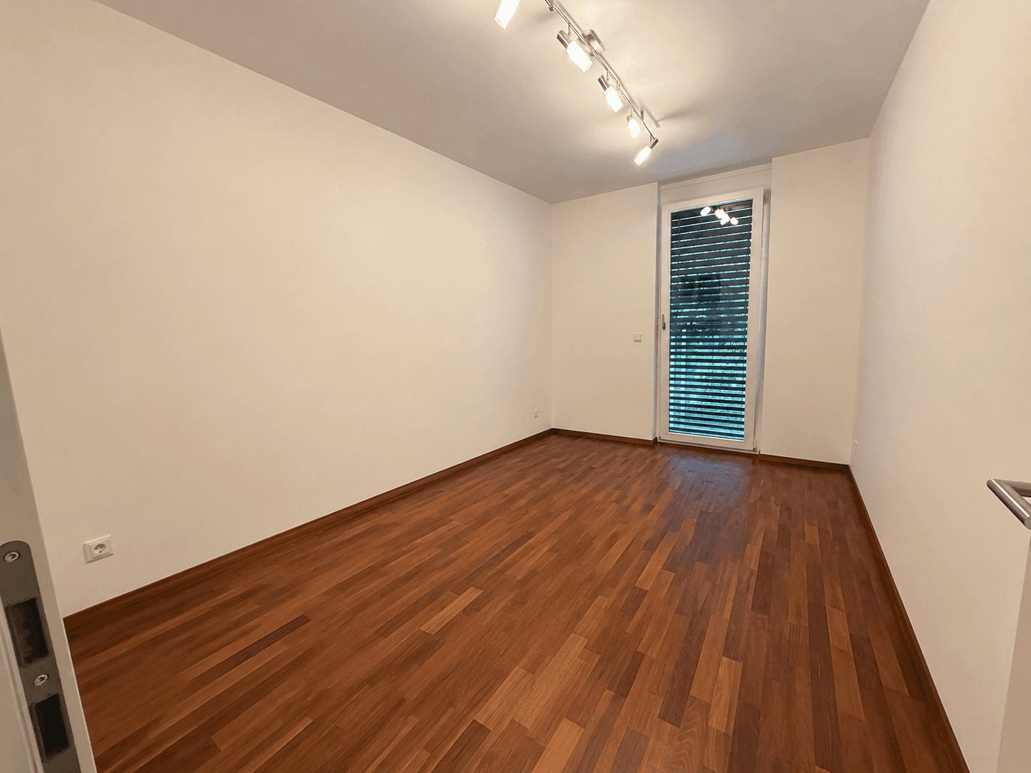 Leeres Zimmer mit Holzboden und großem Fenster, ideal als Schlaf- oder Arbeitszimmer.