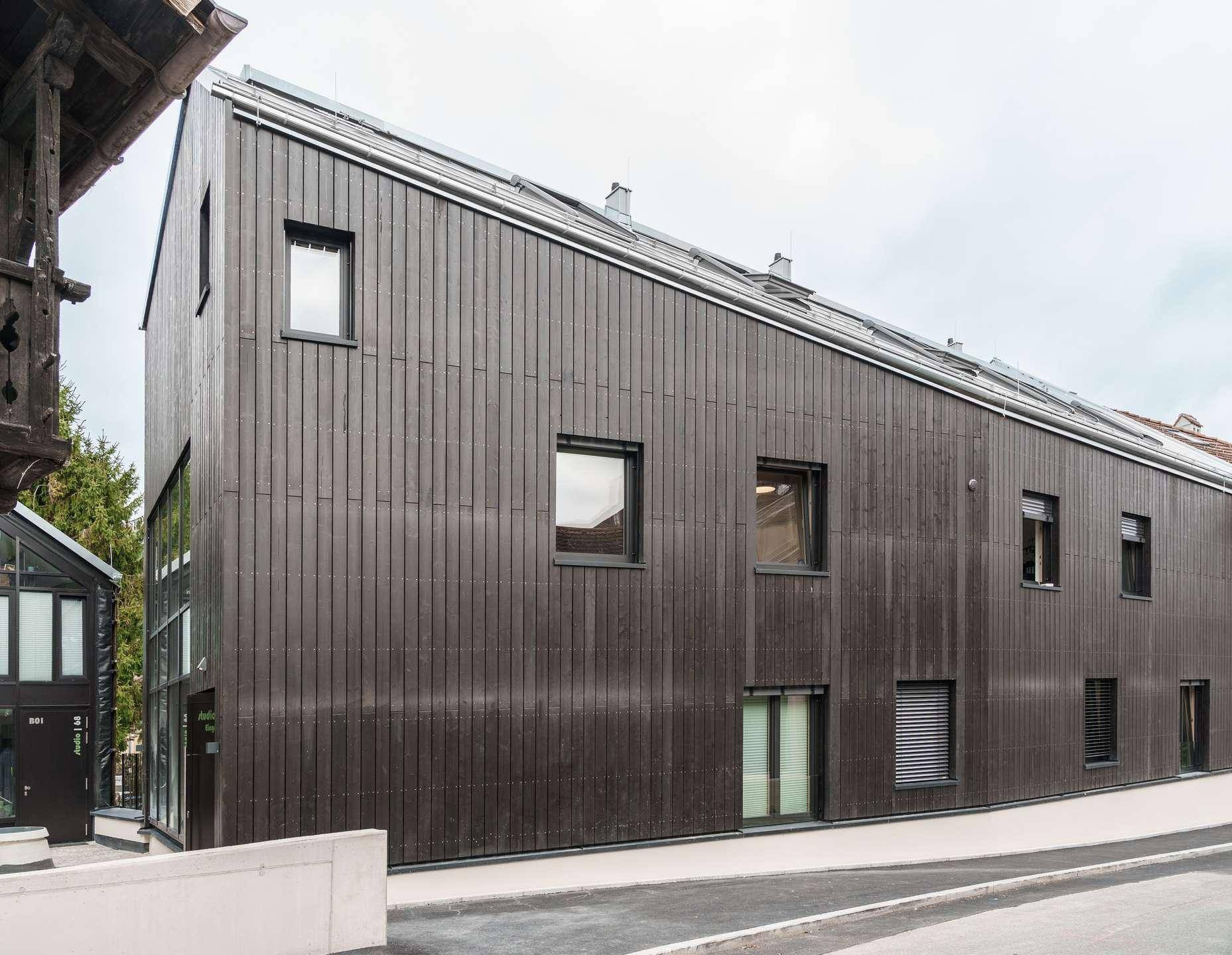 Seitenansicht des modernen Gebäudes mit dunkler Holzfassade und schrägen Dachlinien.