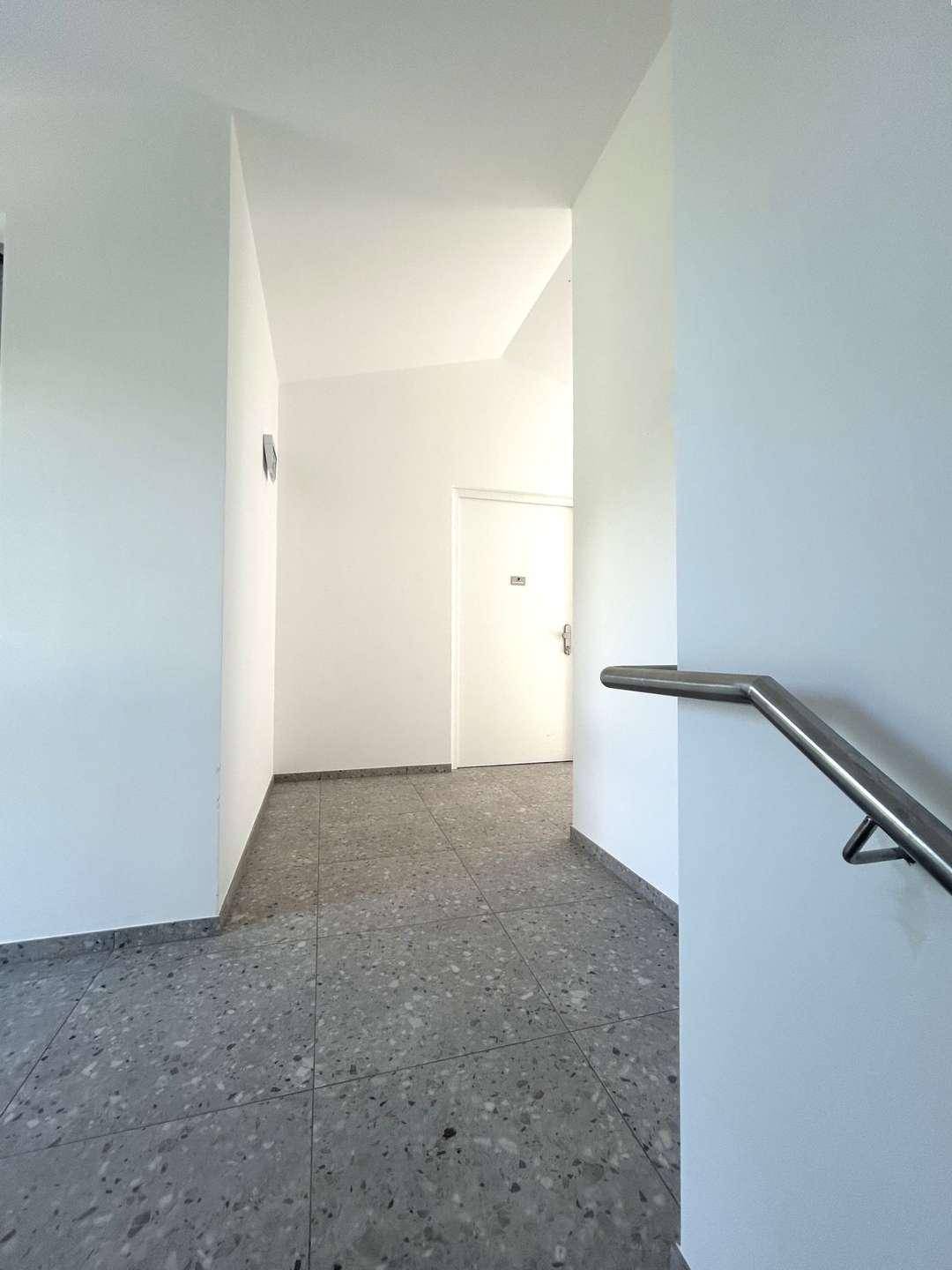 Heller Gemeinschaftsflur mit Terrazzoboden und modernem Metallgeländer.