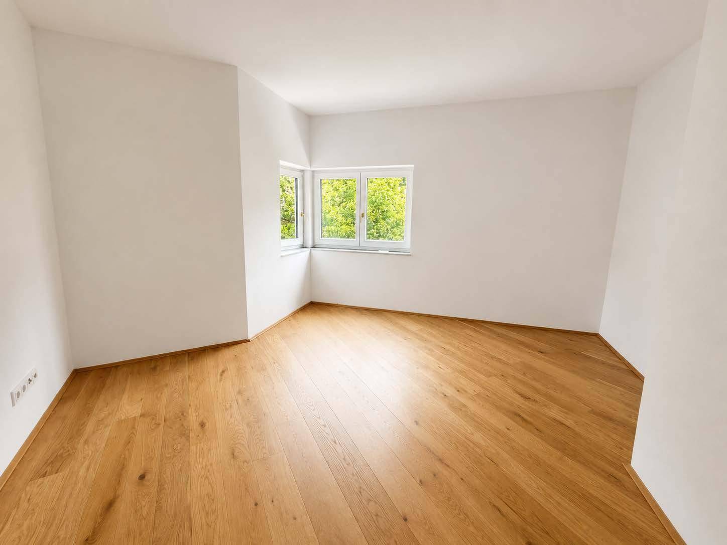 Geräumiges Schlafzimmer mit hellem Parkettboden und Fenstern mit Blick ins Grüne.