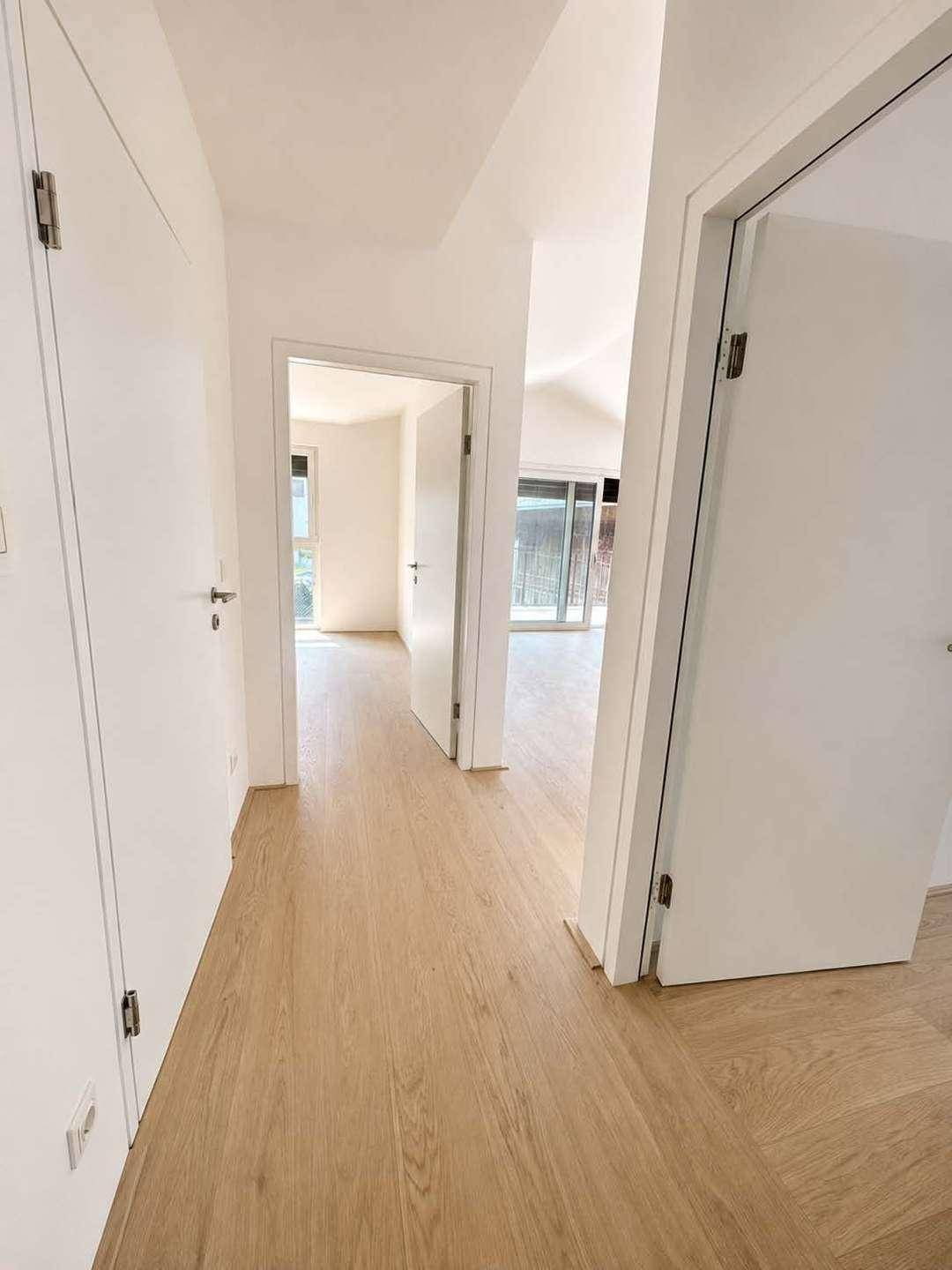 Heller Flur mit Holzboden und weißen Türen, der zu verschiedenen Räumen führt.