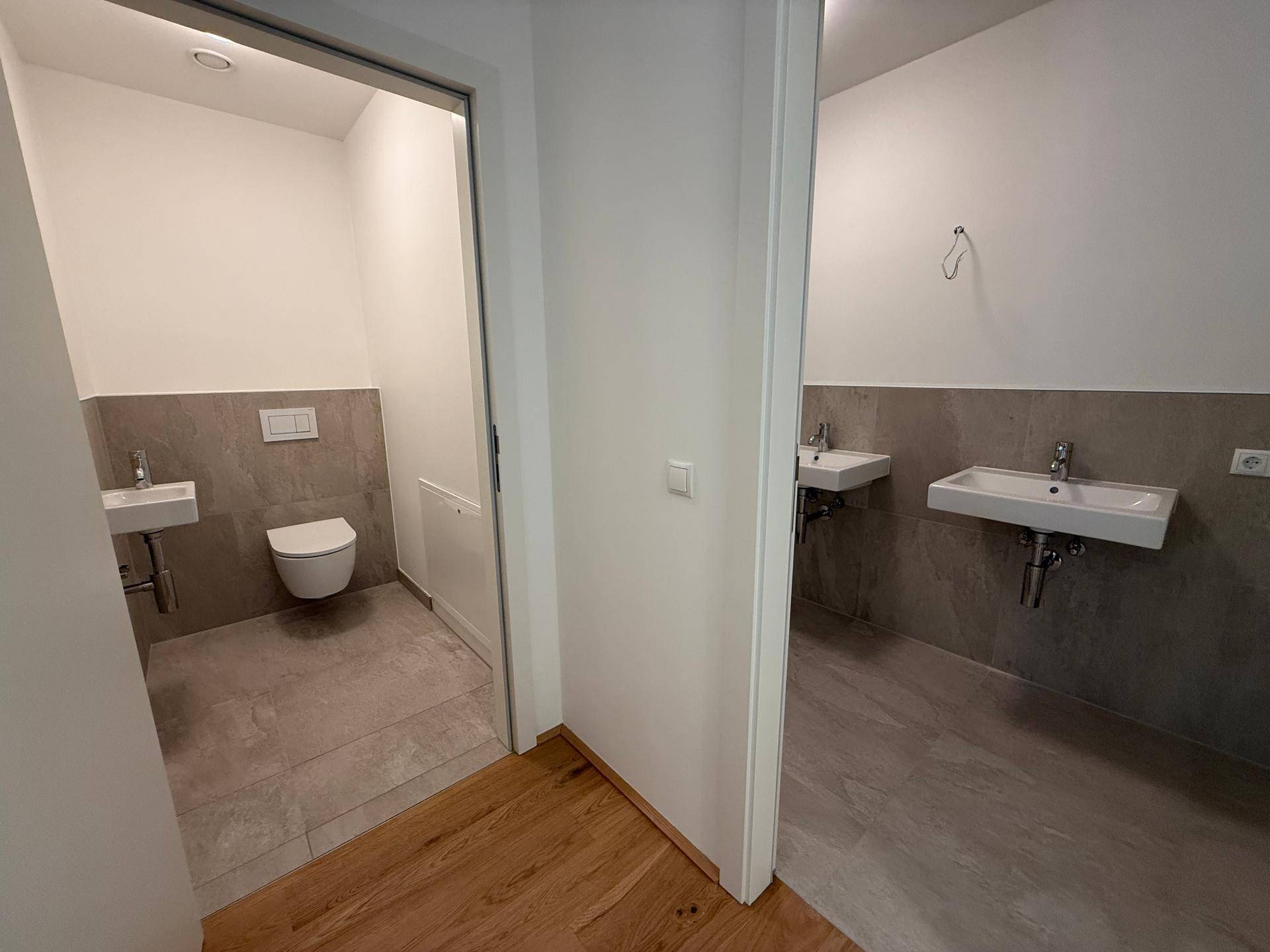 Separates WC mit Wand-WC, kleinem Waschbecken und modernen Fliesen.
