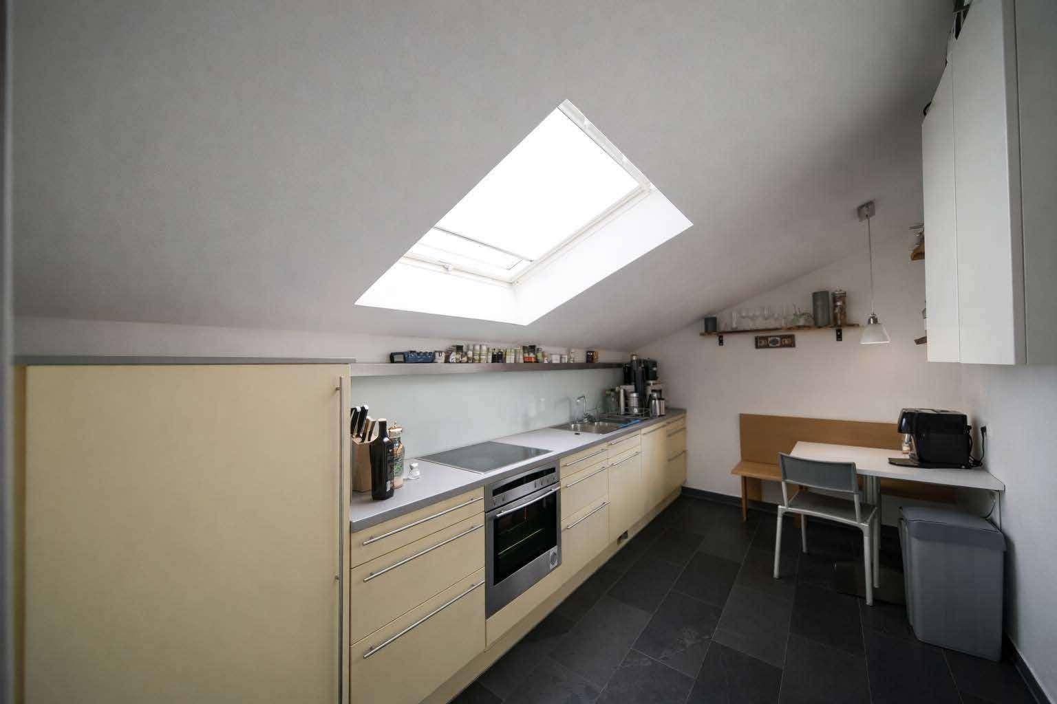 Moderne Küche mit Dachfenster, Einbaugeräten und Essbereich unter der Dachschräge.