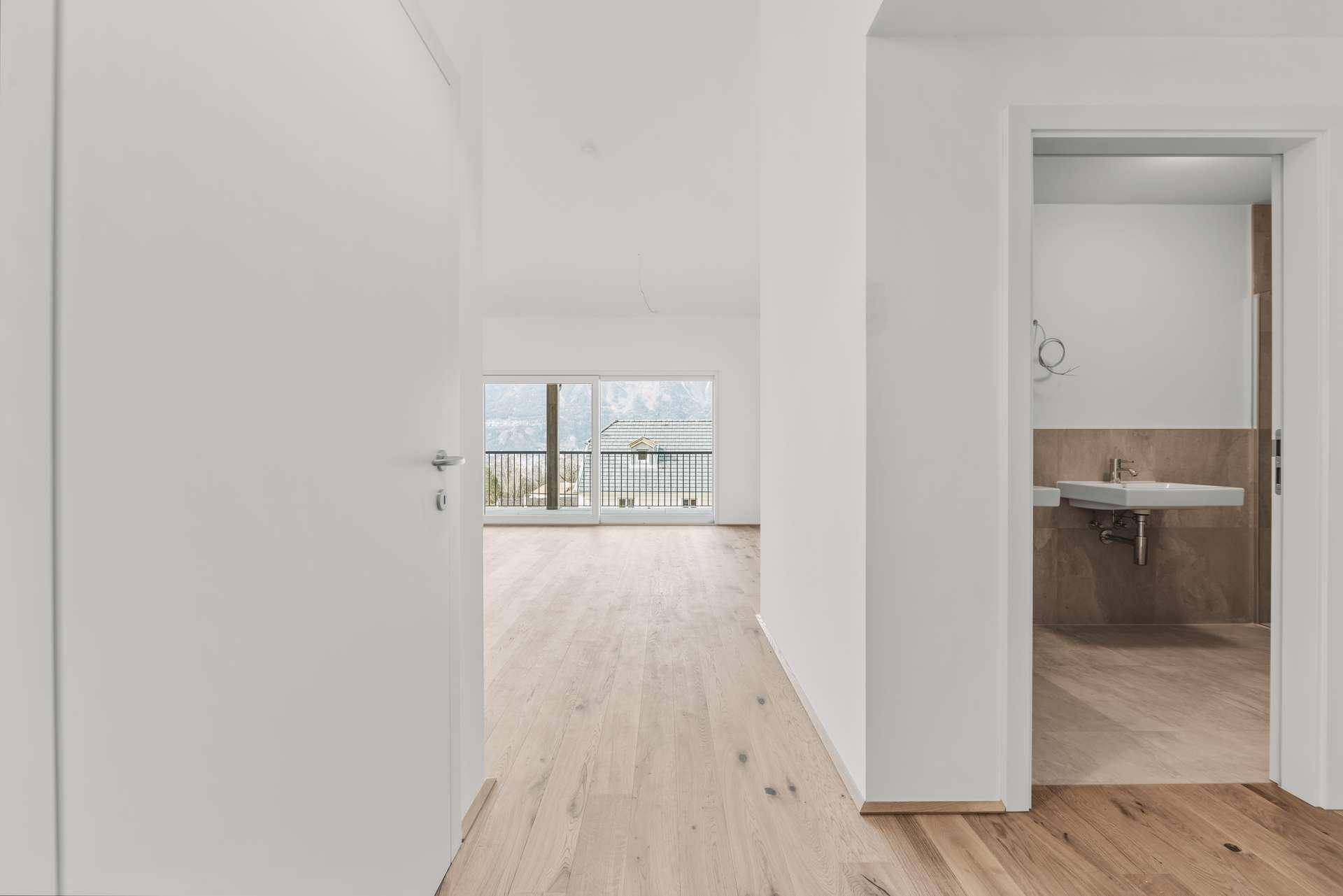 Heller Flur mit Holzboden, der zu einem Zimmer mit Balkon und einem Badezimmer führt.