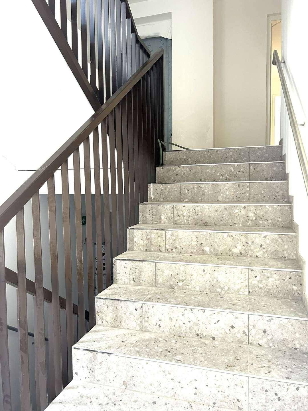 Treppenhaus mit gefliesten Stufen und stabilem Metallgeländer.